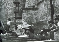 Uczniowie PLSP w Lublinie na plenerze. Dziewczęta i chlopcy stoją lub siedzą wykonując rysunki. W tle mury miasta. I poł. lat 70-tych XX w. Kliknięcie w miniaturkę obrazka spowoduje wyświetlenie powiększonego zdjęcia.