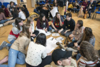 W auli szkolnej młodzież w grupach mieszanych polsko-izraelskich siedzą na podłodze tworząc okręgi. W środku leżą ołówki i arkusze papieru Kliknięcie w miniaturkę obrazka spowoduje wyświetlenie powiększonego zdjęcia.