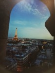 Praca fotograficzna artysty przedstawiająca panoramę Paryża z Wieżą Eiffla. Stoją, siedzą i leżą. W tle obrazy artysty. Kliknięcie spowoduje wyświetlenie powiększonego zdjęcia.