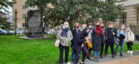Grupa uczniów stoi przed pomnikiem im. Józefa Czechowicza przy ul. Krakowskie Przedmieście w Lublinie. Młodzież jest w maseczkach z powodu obostrzeń sanitarno-epidemiologicznych. Kliknięcie w miniaturkę obrazka spowoduje wyświetlenie powiększonego zdjęcia.