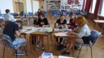 Młodzież rysuje i maluje sceny komiksu w auli szkolnej. Kliknięcie w miniaturkę obrazka spowoduje wyświetlenie powiększonego zdjęcia.
