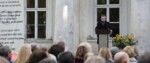 Wicepremier Piotr Gliński stoi przy mikrofonie i mównicy przed Muzeum Cypriana Norwida w Dębinkach. Przemawia do publiczności (widać ich głowy od tyłu). Kliknięcie w miniaturkę obrazka spowoduje wyświetlenie powiększonego zdjęcia.