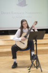 Uczennica gra na gitarze klasycznej w auli szkolnej. Kliknięcie w miniaturkę obrazka spowoduje wyświetlenie powiększonego zdjęcia.
