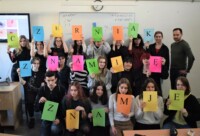 Uczniowie trzymają w rękach pojedyńcze litery tworzące napis: "Czerniak. Znamię? Znam je". Obok stoi Tomasz Banaszkiewicz. Kliknięcie w miniaturkę obrazka spowoduje wyświetlenie powiększonego zdjęcia.