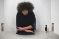 Praca Natalii Pastusiak. Fotografia przedstawia wielką niewyraźną postać siedzącej dziewczyny w czarnym ubraniu w białym pokoju. Obok stoi mała postać tej samej dziewczyny. Kliknięcie w miniaturkę obrazka spowoduje wyświetlenie powiększonego zdjęcia.