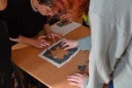 Uczniowie składają układankę z papieru na stole w auli. Rozwiązują zadanie konkursowe. Kliknięcie w miniaturkę obrazka spowoduje wyświetlenie powiększonego zdjęcia.